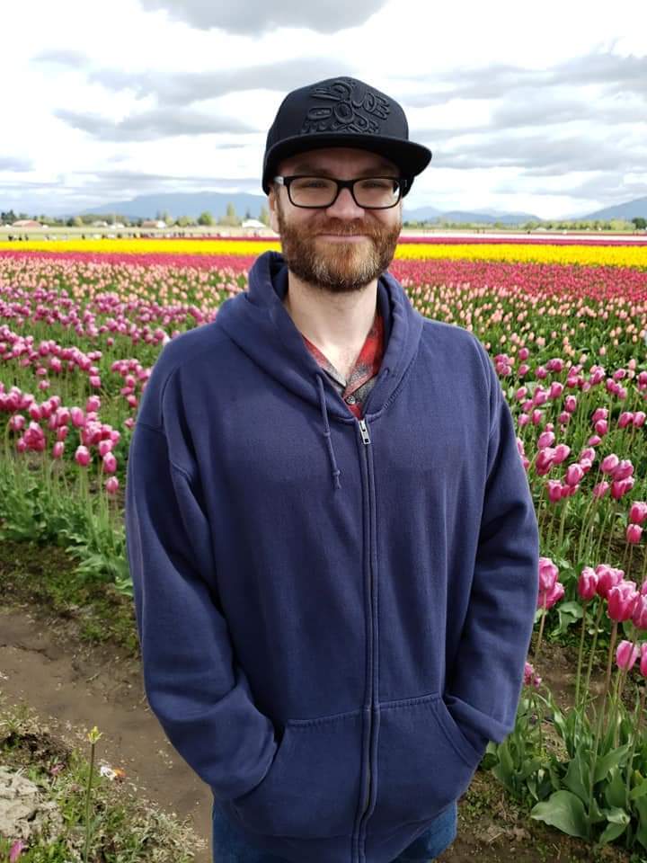 Joshua Heath, in a black cap and glasses, standing in a field of tulips